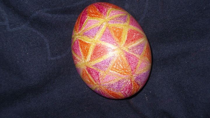 Ein bunt bemaltes Osterei mit geometrischem Muster liegt auf dunklem Stoff.