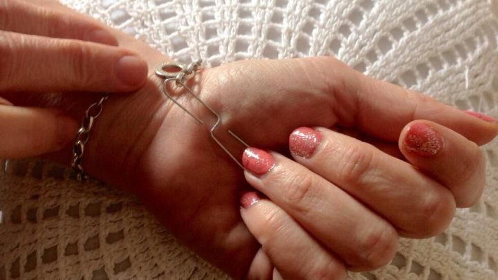 Eine Hand mit einem Armband wird mit einer anderen Hand angezogen, auf einem strukturierten, hellen Untergrund.