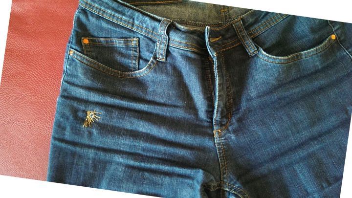 Jeans mit einem Loch, das mit bunter Stickerei verdeckt ist, liegen auf einem roten Untergrund.