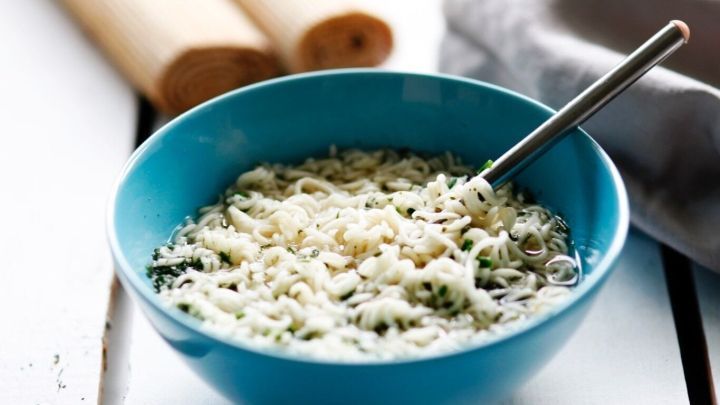 Eine helle Sch&uuml;ssel mit Yum Yum Nudeln steht auf einem Tisch. Ein L&ouml;ffel r&uuml;hrt die Nudeln unter, w&auml;hrend eine graue Serviette daneben liegt.