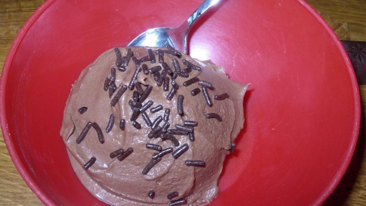 Ein Schokoladen-Sorbet befindet sich in einer roten Sch&uuml;ssel, garniert mit Schokoladensp&auml;nen, bereit zum Genie&szlig;en.