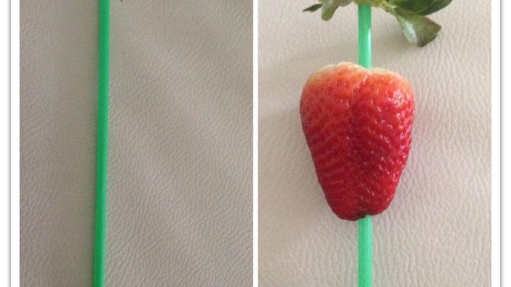 Ein gr&uuml;ner Trinkhalm, der in eine Erdbeere eingef&uuml;hrt wird, um den Erdbeerstrunk zu entfernen.