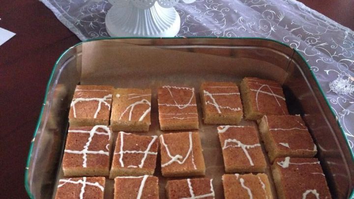 In einer Glasform liegen schmackhafte Blondies mit wei&szlig;er Schokolade, dekoriert mit einer Zuckerglasur, auf einem Tisch.