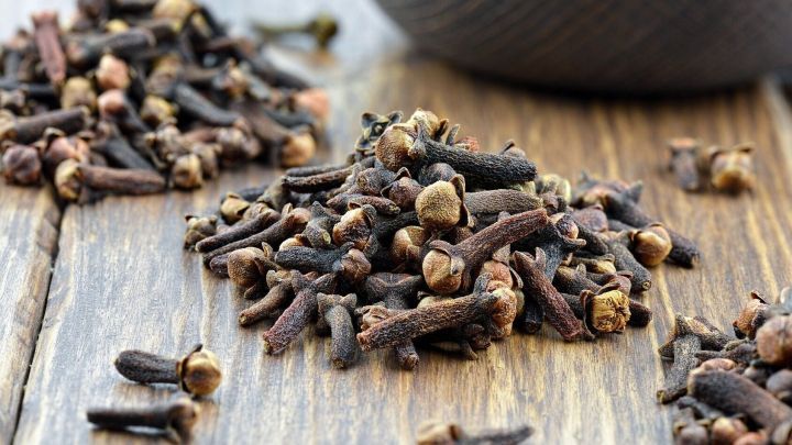 Nelken liegen verstreut auf einem Holzuntergrund, w&auml;hrend eine Sch&uuml;ssel im Hintergrund steht. Sie k&ouml;nnen zur Ameisenbek&auml;mpfung verwendet werden.