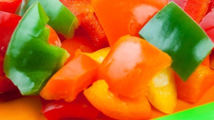 Bunte, geschnittene Paprika liegen in einem Beutel, w&auml;hrend ein gr&uuml;nes K&uuml;chenmesser zur Seite platziert ist.