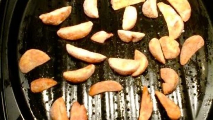 Knusprige, kalorienarme Pommes frittieren auf einem Grill, verteilt auf einer schwarzen Grillplatte in einer K&uuml;che.