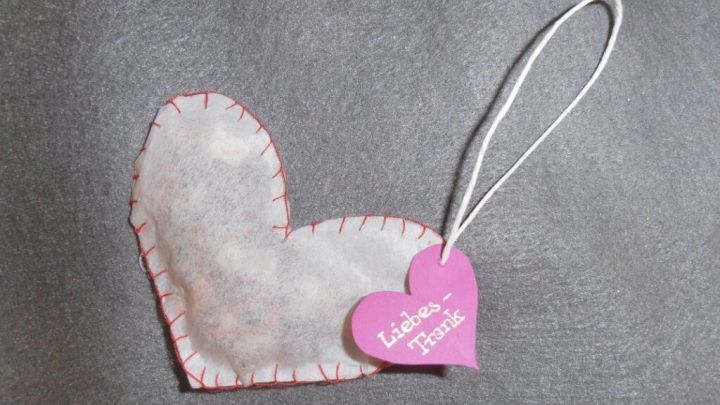 Ein handgemachter Teebeutel in Herzform liegt auf einer grauen Unterlage, versehen mit einem rosa Anh&auml;nger f&uuml;r Tees.