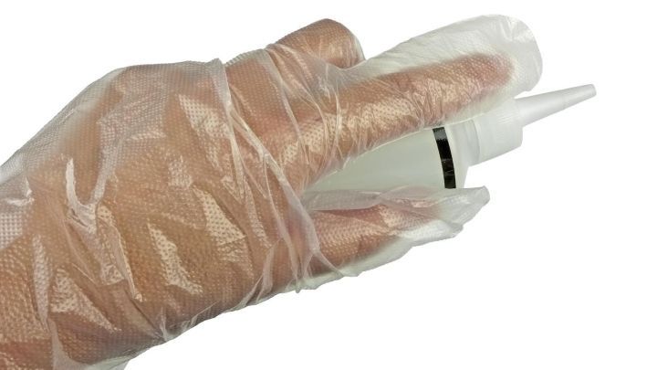 Eine Hand tr&auml;gt Einweghandschuhe und h&auml;lt eine Flasche mit einer Spritzaufsatz, bereit zur Anwendung.