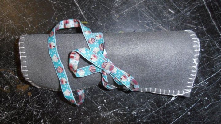 Eine graue Filzrolle mit buntem Band, die zusammengebunden ist, dient zur Aufbewahrung von Stiften oder Pinseln.