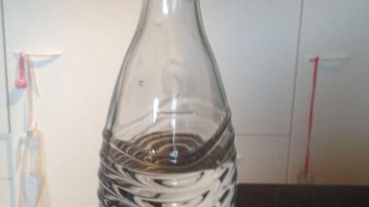 Eine Glasflasche steht auf einem Tisch und enth&auml;lt Wasser. Der Hintergrund ist hell und schlicht gehalten.