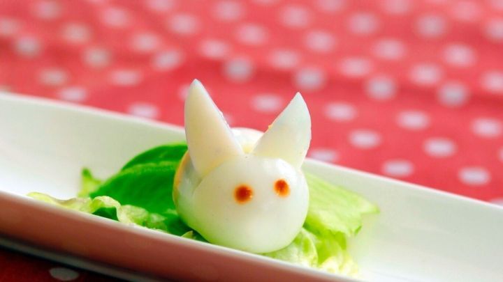 Ein niedliches H&auml;schen aus Ei liegt auf einem gr&uuml;nen Salatblatt, umgeben von einem rot gepunkteten Hintergrund.