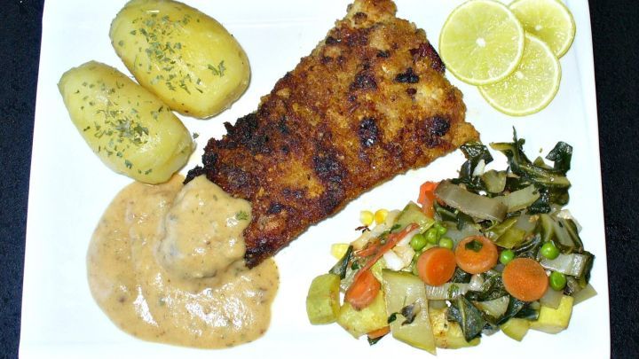 Fisch-Cordon bleu auf Teller mit Petersilienkartoffeln, gemischtem Gem&uuml;se und Zitronenscheiben in heller So&szlig;e angerichtet.