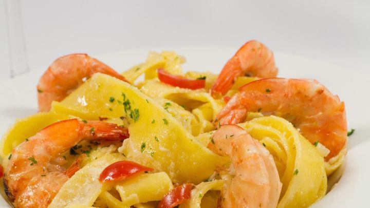 Safran-Bandnudeln liegen kunstvoll auf einem Teller, umgeben von Garnelen und einer cremigen Dill-Sahne-Curry-So&szlig;e.