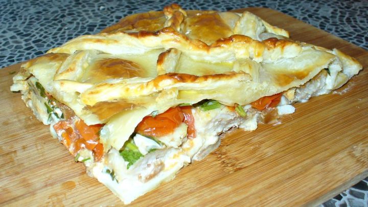 Ein goldbraunes Fischfilet im Bl&auml;tterteigmantel liegt auf einem Holzbrett, umgeben von frischen Gem&uuml;se-Scheiben.