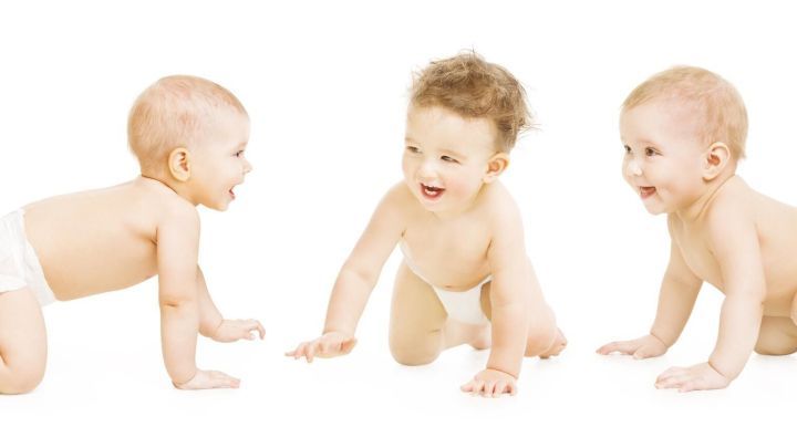 Drei fr&ouml;hliche Babys krabbeln auf einem wei&szlig;en Untergrund, erkunden neugierig ihre Umgebung und spielen miteinander.