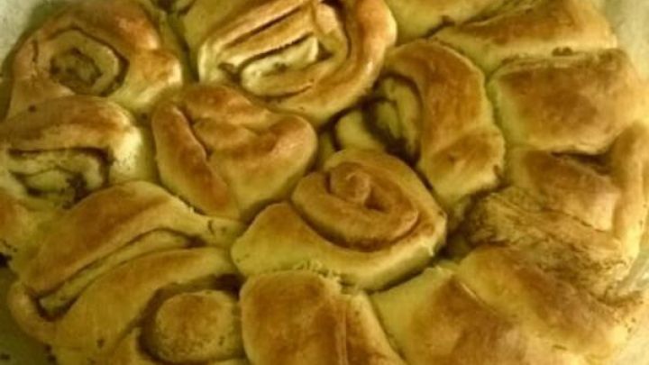 Ein frisch gebackener Zimtschneckenkuchen liegt auf Backpapier, mit goldbrauner Oberfl&auml;che und sichtbaren Zimtschnecken.