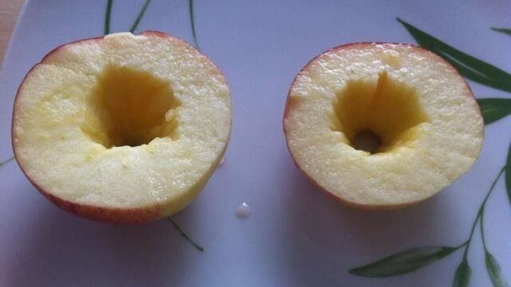 Zwei halbierte &Auml;pfel auf einem Teller zeigen die hohlen Innenr&auml;ume, bereit f&uuml;r die F&uuml;llung mit Karamellkern.