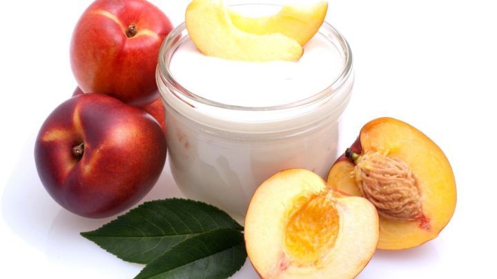 Eine Quarkspeise steht neben frischen Fr&uuml;chten, darunter &Auml;pfel und Pfirsiche, auf einem wei&szlig;en Hintergrund.