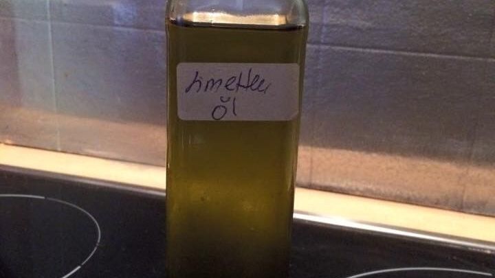 Eine Flasche mit gr&uuml;nlichem &Ouml;l steht auf einem schwarzen Kochfeld, beschriftet mit "Smeille &Ouml;l".