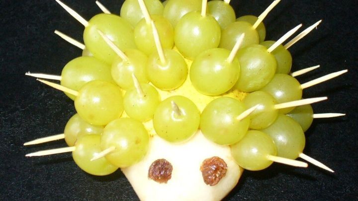Ein kreativer Birnenigel mit gr&uuml;nen Trauben, spitzen Zahnstochern und einer s&uuml;&szlig;en Gesichtsgestaltung auf einem schwarzen Hintergrund.