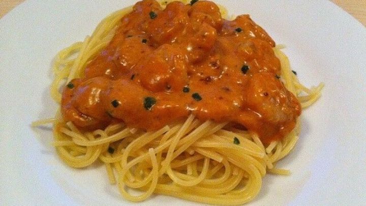 Spaghetti liegen auf einem wei&szlig;en Teller, bedeckt mit einer cremigen Garnelen-Sauce, garniert mit Kr&auml;utern.