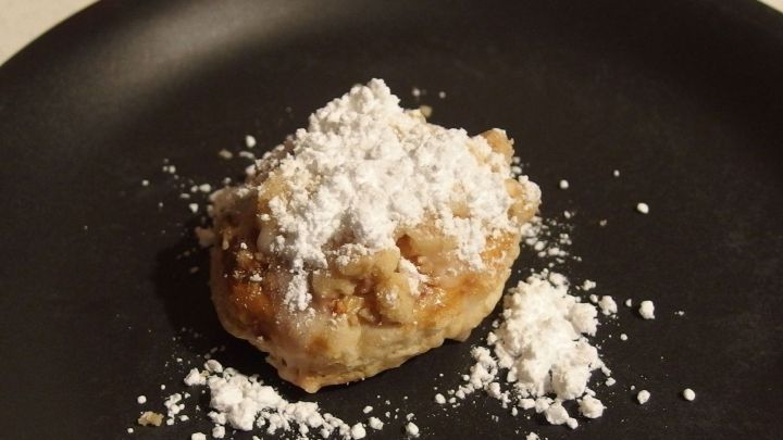 Streuselzungen aus Bl&auml;tterteig liegen auf einem schwarzen Teller, mit Puderzucker best&auml;ubt, in einer gem&uuml;tlichen K&uuml;che.