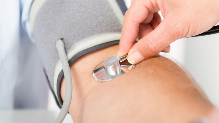 Eine Hand legt ein Blutdruckmessger&auml;t an den Arm, um Bluthochdruck zu &uuml;berpr&uuml;fen, w&auml;hrend der Arzt assistiert.