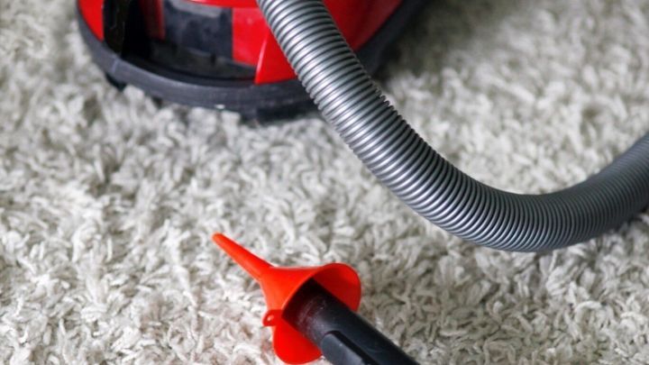 Ein roter Staubsauger steht auf einem Teppich, w&auml;hrend eine alternative Staubsaugerd&uuml;se daneben liegt.