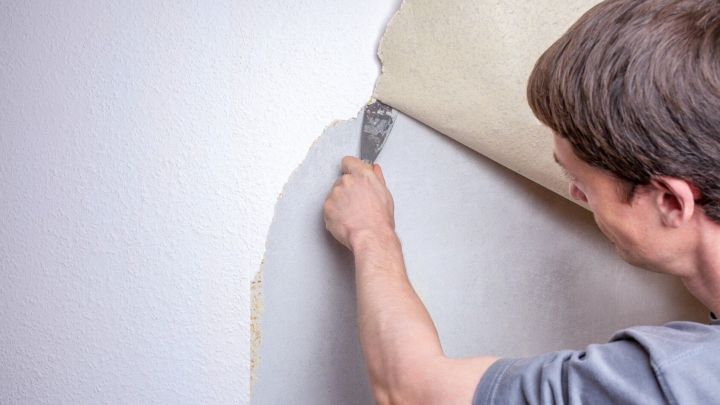 Eine Person entfernt aufmerksam eine Tapete von der Wand, um m&uuml;helos ihr Zuhause zu renovieren.