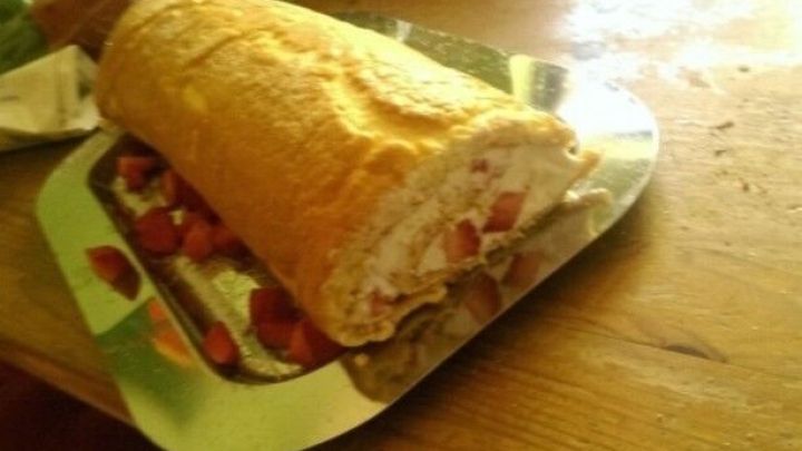 Eine Low Carb Erdbeerrolle liegt auf einem silbernen Teller, umgeben von frischen Erdbeeren auf einem Holztisch.