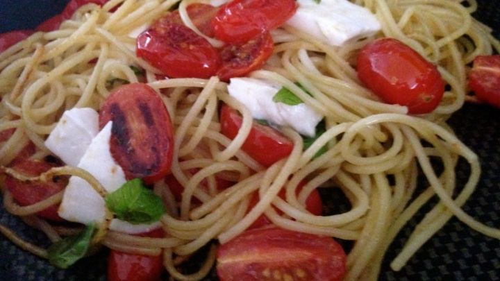 Spaghetti mit frischen Tomaten und Mozzarella werden angerichtet, umgeben von einem dunklen Teller.