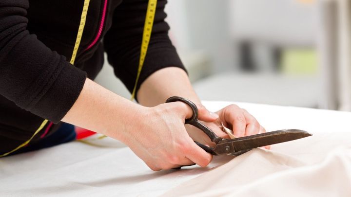 Ein Esstisch wird als Zuschneidetisch genutzt, w&auml;hrend jemand mit einer Schere Stoff pr&auml;zise zuschneidet.