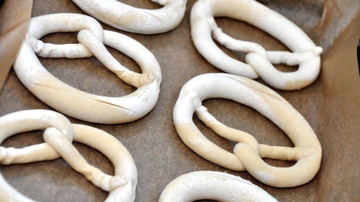 Sechs ungebackene Brezeln liegen auf Backpapier und warten darauf, im Ofen gebacken zu werden. Backpapier sparen ist wichtig.