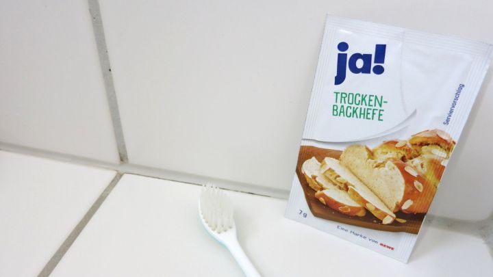 Eine T&uuml;te mit Hefe steht neben einem wei&szlig;en L&ouml;ffel auf wei&szlig;en Fliesen, ideal zum Einsatz gegen Schimmel in Fugen.