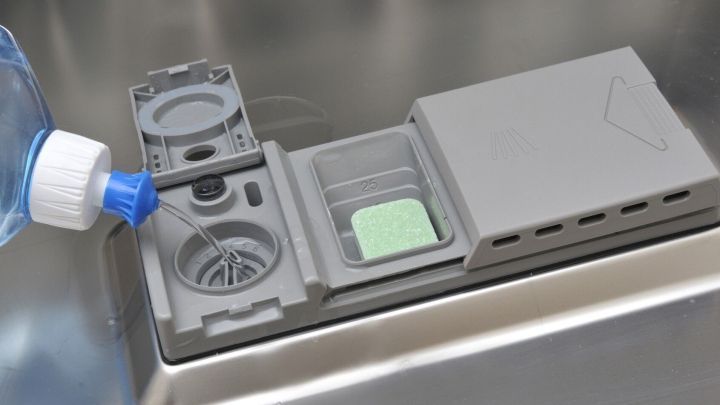 Eine Glas-Herdabdeckplatte wird mit einem Reinigungsmittel aus einer Flasche behandelt, w&auml;hrend sie in einer modernen K&uuml;che platziert ist.