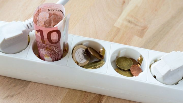 Eine Steckdose ist mit einem 10-Euro-Schein und Kleingeld gef&uuml;llt, um die hohen Stromkosten im Haushalt zu veranschaulichen.
