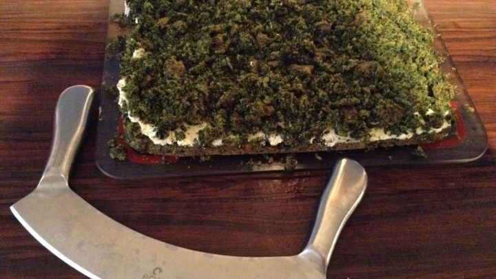 Ein Wiegemesser liegt neben einem Blech mit mit Kr&auml;utern belegter Pizza, bereit, die Pizza zu schneiden.