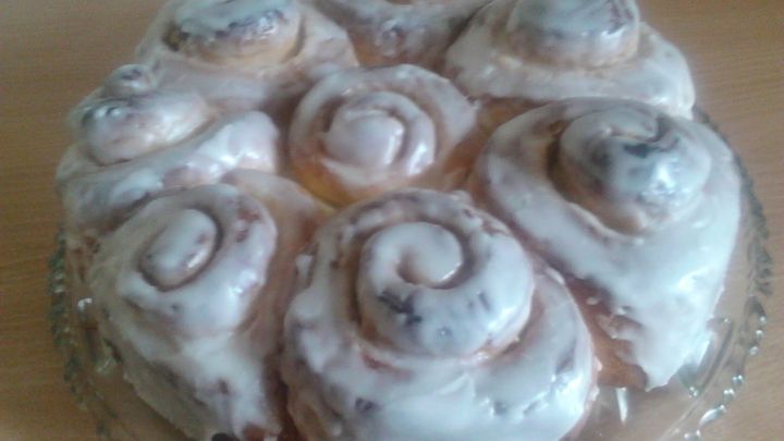 Ein Rosenkuchen mit Zuckerguss liegt auf einem Glasteller auf einem Holztisch.