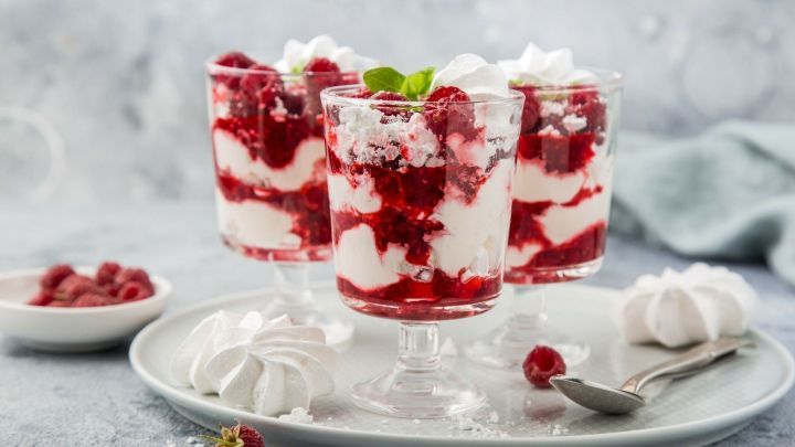 Himbeertraum in Gl&auml;sern schichtet Himbeeren, Baiser und Sahne, angerichtet auf einem Teller neben frischen Beeren.