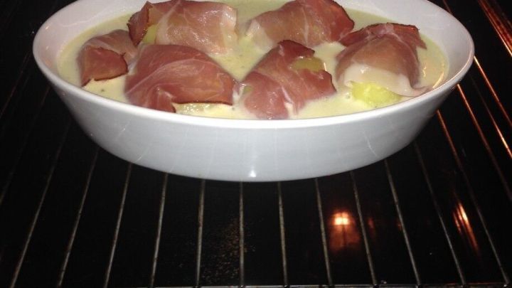 Im Backofen garen Kartoffeln im Baconmantel, umgeben von einer cremigen Zitronen-Sahne-So&szlig;e in einer wei&szlig;en Auflaufform.