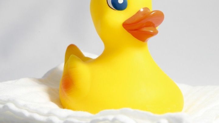 Eine gelbe Gummiente sitzt auf einem Stapel wei&szlig;er Mullwindeln, die sauber und ordentlich angeordnet sind.