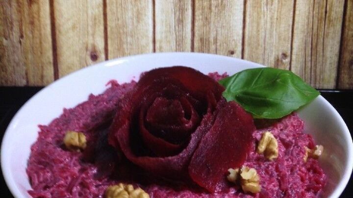 Ein bunter Rote Bete Salat liegt in einer Sch&uuml;ssel, dekoriert mit einer Rosenschicht und Waln&uuml;ssen, vor rustikalem Holz.