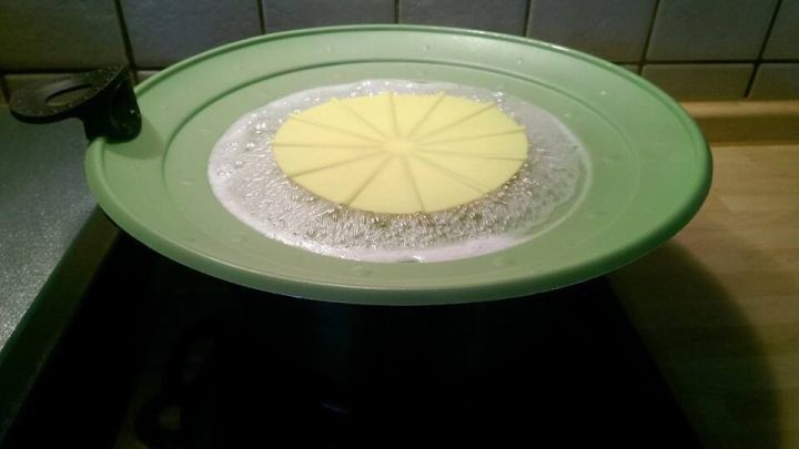 Ein gr&uuml;ner &Uuml;berkochschutz liegt auf einem Topf, der kochenden Inhalt zeigt, ohne dass es &uuml;berkocht, in einer K&uuml;che.