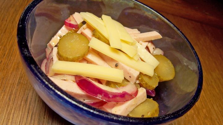 Ein bunter Wurstsalat liegt in einer Sch&uuml;ssel, bestehend aus Wurst, K&auml;se und eingelegten Gurken.