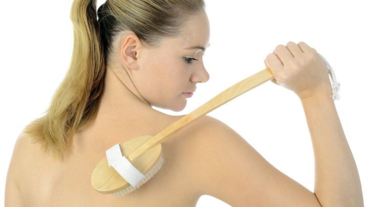 Eine Frau cremt ihren R&uuml;cken mit einem langen Pinsel ein, um schwer erreichbare Stellen in einem hellen Raum zu behandeln.