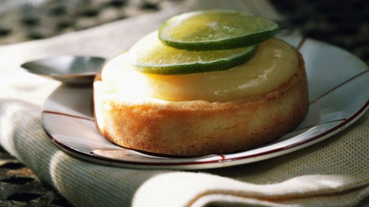 Eine Limettentarte ruht auf einem dekorativen Teller, belegt mit zwei Scheiben Limette und begleitet von einem L&ouml;ffel.