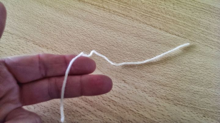 Eine Hand h&auml;lt einen vergr&ouml;&szlig;erbaren Maschenmarkierer aus Wolle an einem Tisch, bereit zum Einsatz beim Stricken.