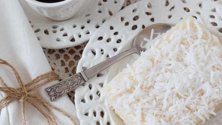 Ein luftiger Kokoskuchen liegt auf einem dekorativen Teller neben einer Tasse schwarzem Kaffee in einem gem&uuml;tlichen Setting.