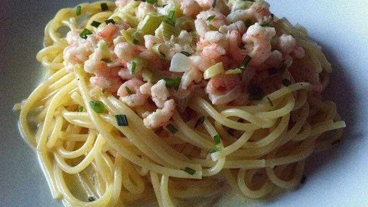 Pasta mit Shrimps liegt auf einem wei&szlig;en Teller, umgeben von frischen Kr&auml;utern und sieht appetitlich aus.
