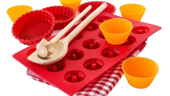 Silikonbackformen liegen auf einem karierten Tuch, umgeben von bunten F&ouml;rmchen und Holzutensilien zur Zubereitung.